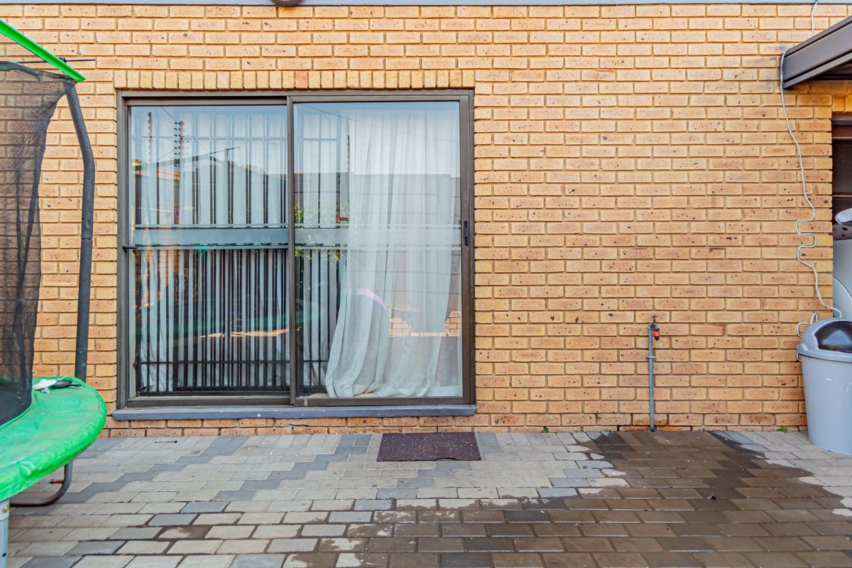 A rear exterior view of the townhouse featuring a paved patio area, brick wall construction, and a sliding glass door with security bars.