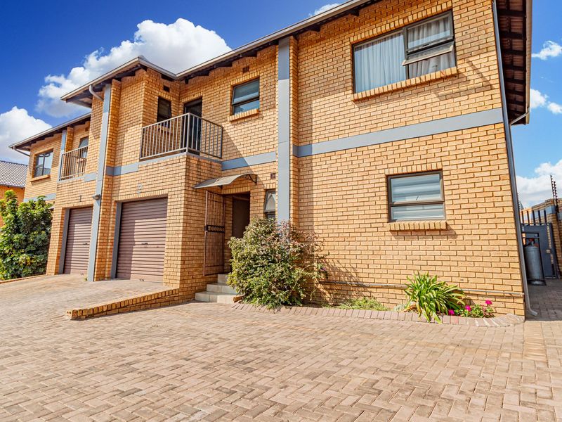 Front elevation of a multi-story brick townhouse featuring a paved driveway, integrated garages, and a balcony.
