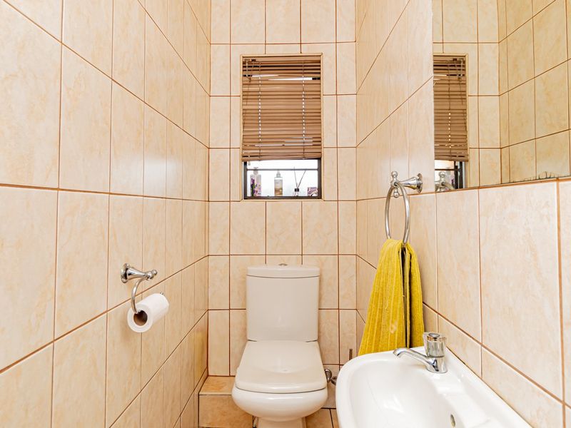 A compact guest bathroom featuring floor-to-ceiling ceramic tiling, a pedestal basin, and a standard toilet, finished with chrome fixtures and a wall-mounted mirror.