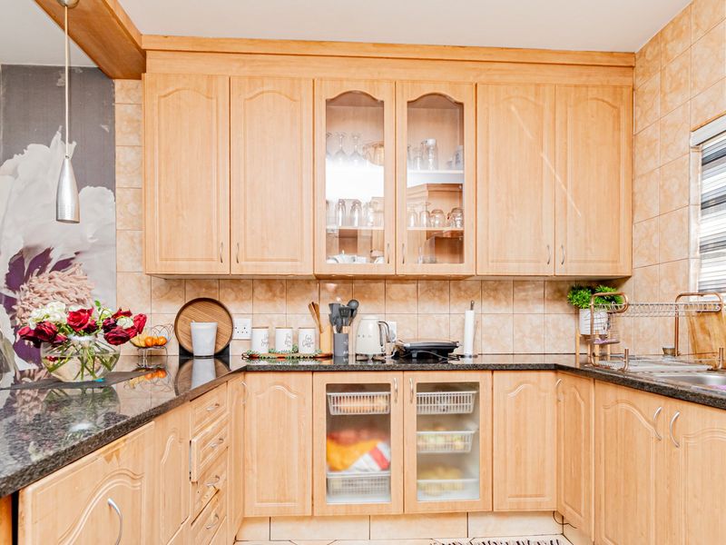 A functional kitchen featuring light wood-finish cabinetry, dark granite countertops, and tiled wall finishes with integrated storage solutions.