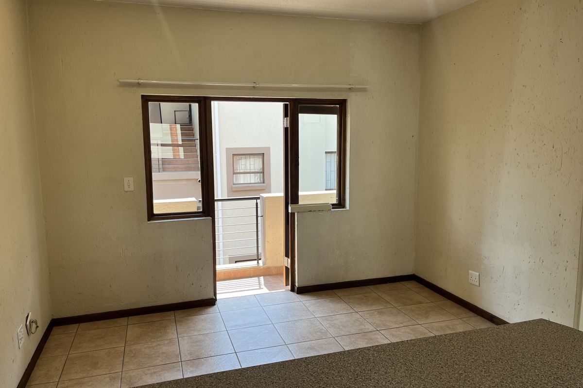 An empty living area featuring tiled flooring and a sliding door leading to a balcony, with walls requiring cosmetic attention.