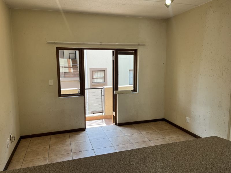 An empty living area featuring tiled flooring and a sliding door leading to a balcony, with walls requiring cosmetic attention.