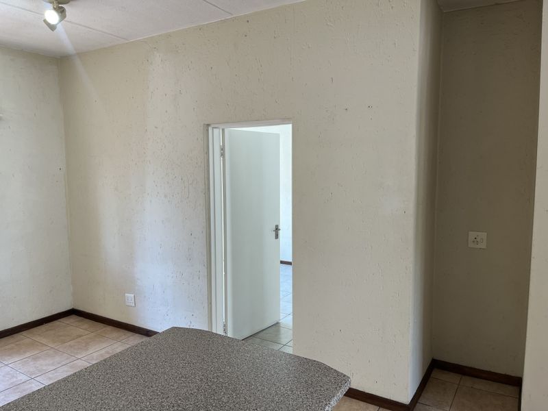 An empty open-plan living area featuring tiled flooring, neutral textured walls, and a doorway leading to an adjacent room.