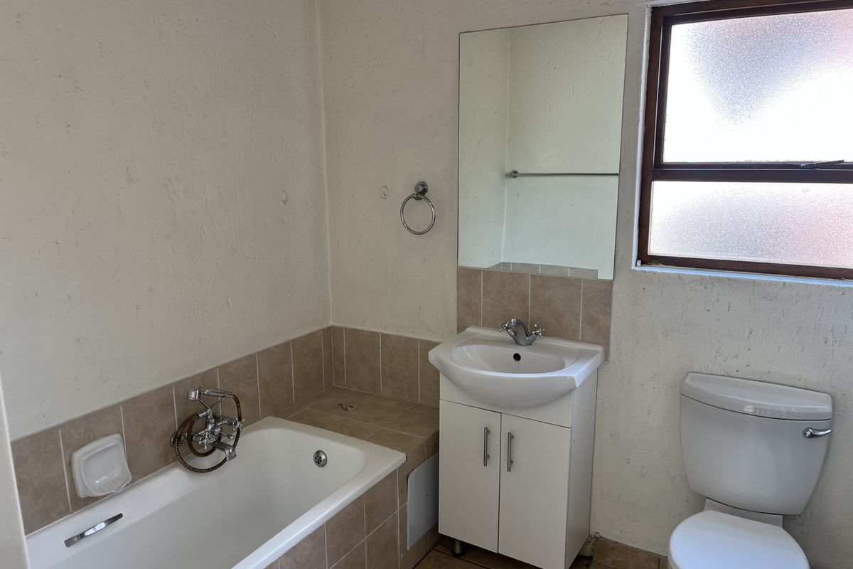 A functional bathroom featuring a built-in bathtub, vanity cabinet with basin, and toilet, finished with tiled flooring and splashbacks.