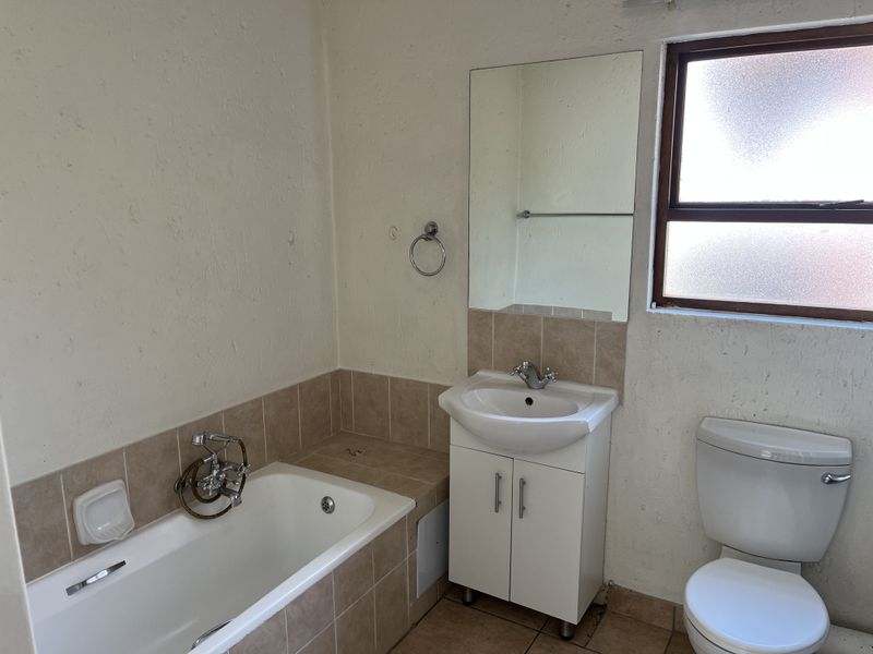 A functional bathroom featuring a built-in bathtub, vanity cabinet with basin, and toilet, finished with tiled flooring and splashbacks.