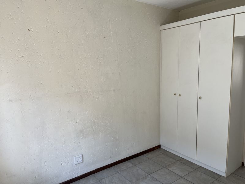 A bedroom featuring tiled flooring and a built-in white wardrobe, requiring cosmetic updates to the wall finishes.