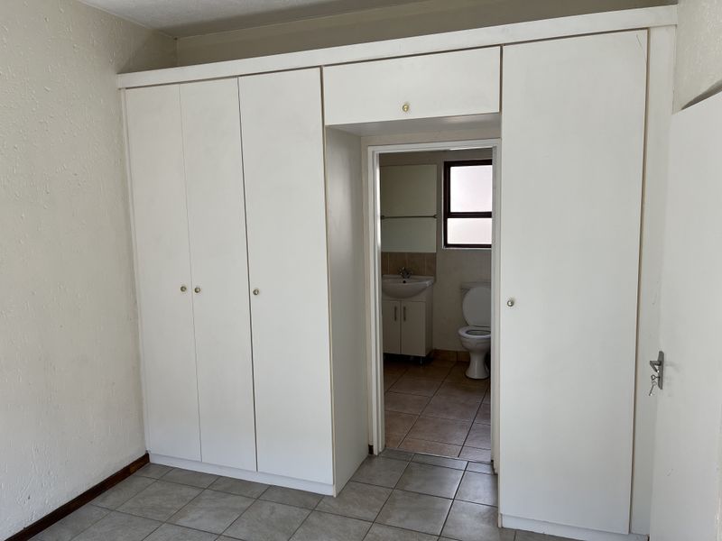 Bedroom featuring built-in white cupboards and direct access to an en-suite bathroom with tiled flooring throughout.