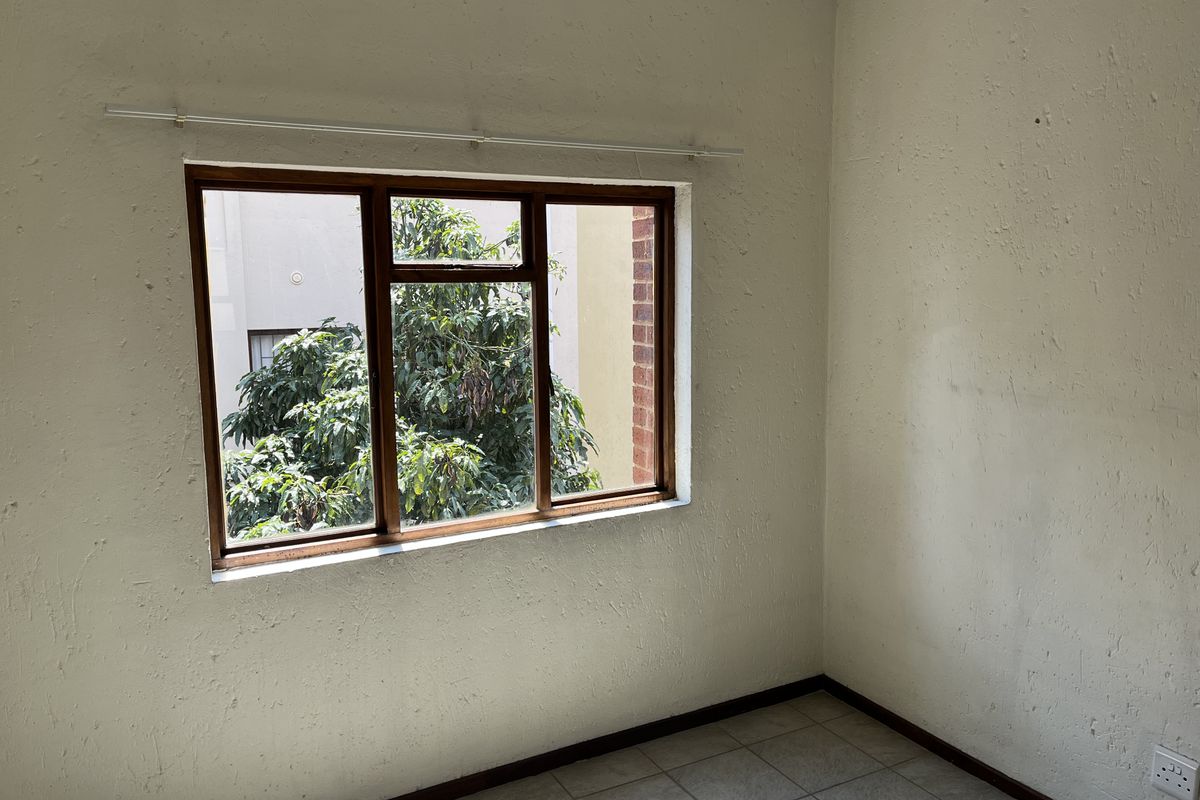 An empty bedroom featuring tiled flooring and a timber-framed window, requiring cosmetic updates to the wall finishes.