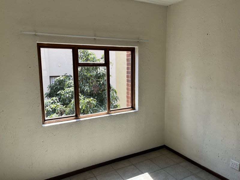 An empty bedroom featuring tiled flooring and a timber-framed window, requiring cosmetic updates to the wall finishes.