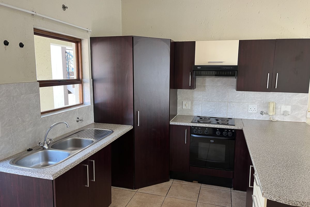 A functional kitchen featuring dark wood cabinetry, laminate countertops, a built-in oven with hob, and a double bowl stainless steel sink.