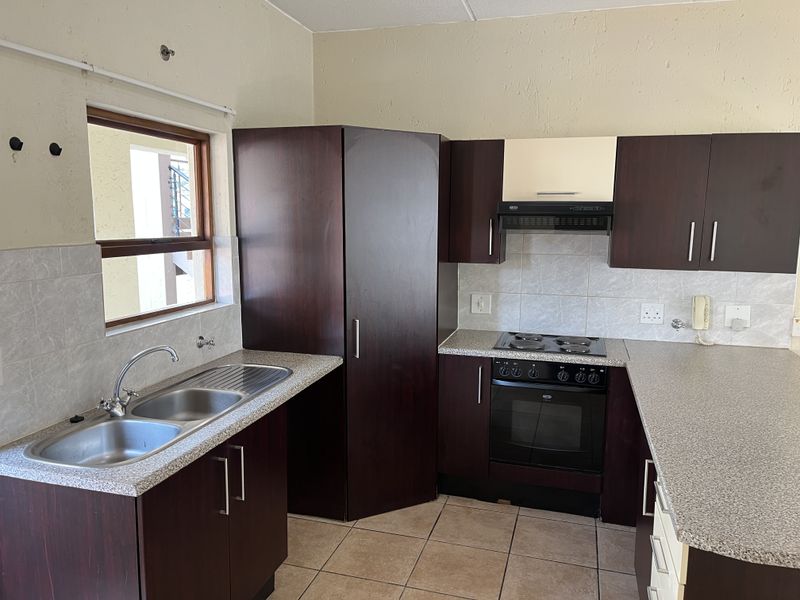 A functional kitchen featuring dark wood cabinetry, laminate countertops, a built-in oven with hob, and a double bowl stainless steel sink.