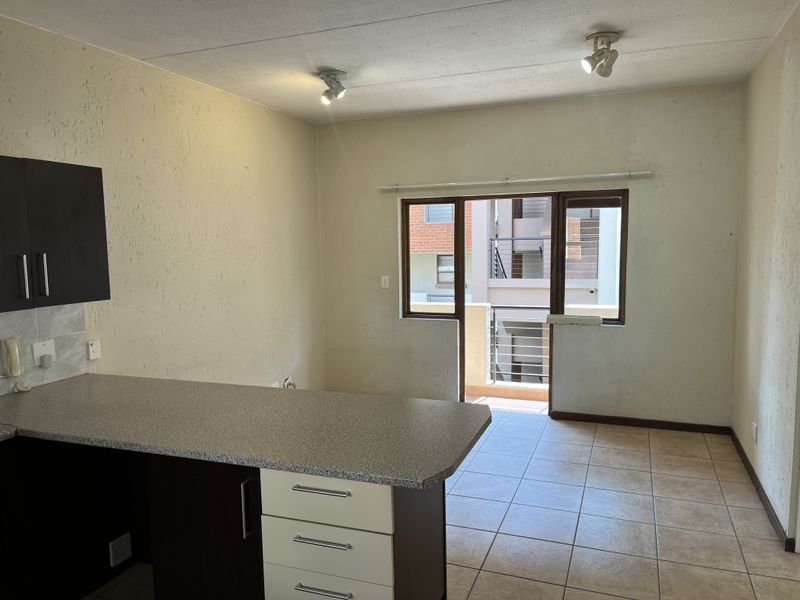 Open plan living area featuring a kitchen with dark cabinetry, laminate countertops, ceramic tiled flooring, and access to a private balcony.