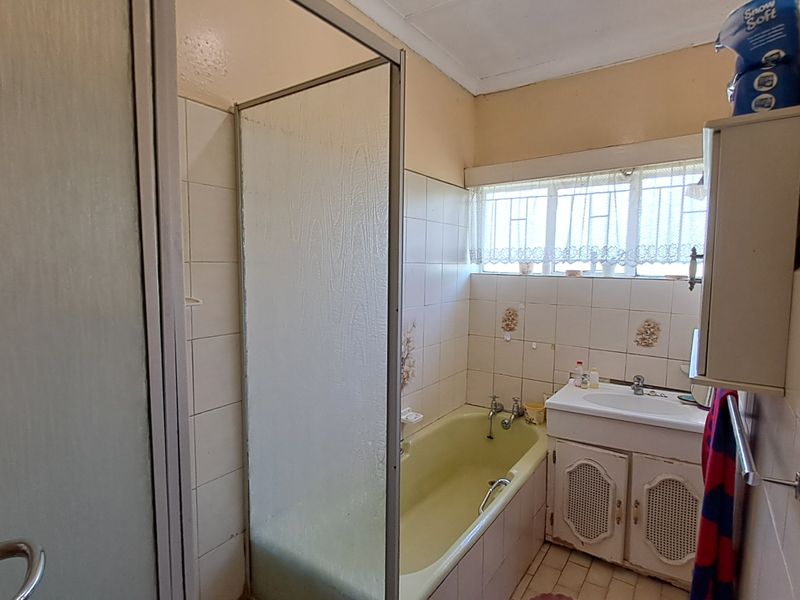 A dated bathroom featuring a built-in vanity, bathtub with shower screen, and tiled walls, currently requiring cosmetic updates and wall repairs.