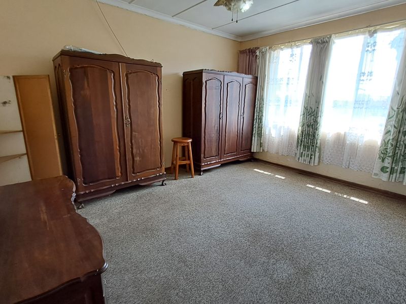 A spacious bedroom featuring carpeted flooring, large windows for natural light, and built-in shelving, offering a blank canvas for renovation and modernization.