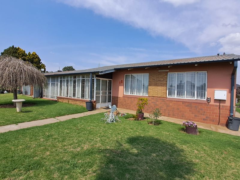 Rear view of a single-story brick house featuring a metal roof, security-barred windows, and a well-maintained lawn with a concrete pathway.