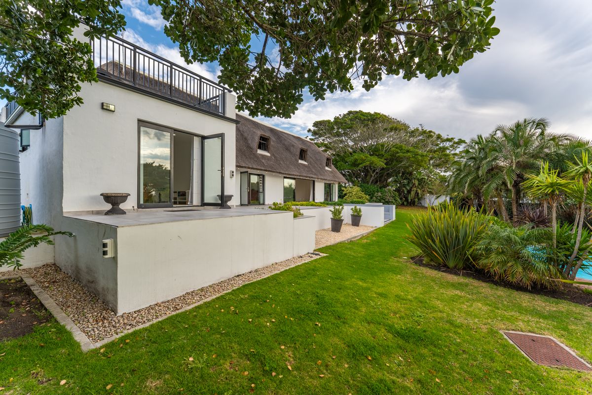 Rear view of a thatched-roof house featuring a tiled patio, balcony with metal railing, and well-maintained garden area.