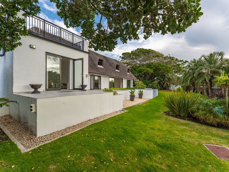 Rear view of a thatched-roof house featuring a tiled patio, balcony with metal railing, and well-maintained garden area.