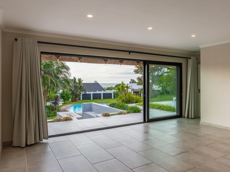 Spacious living area featuring large sliding glass doors that open onto a patio with pool views, finished with neutral floor tiles and recessed lighting.