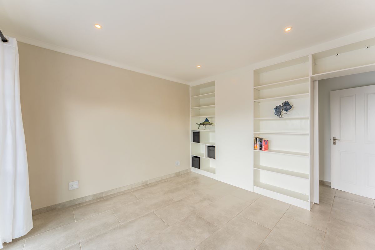 A bright, empty bedroom featuring neutral tiled flooring, recessed downlights, and extensive built-in white shelving units.