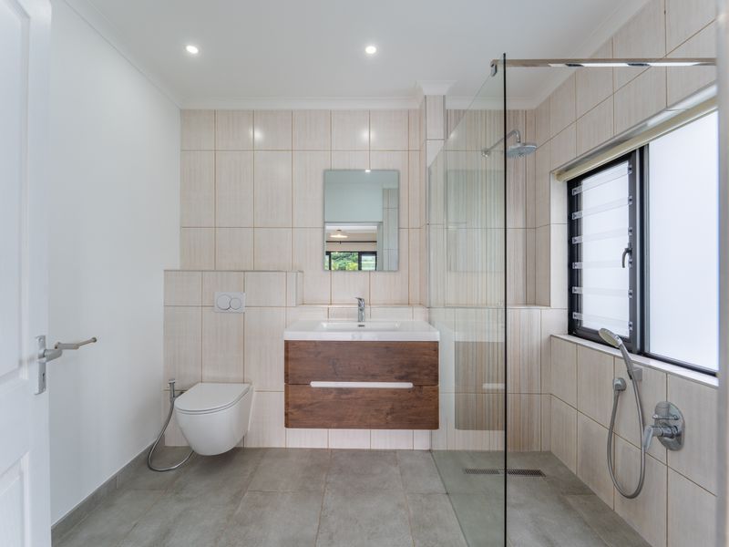 Modern bathroom featuring a floating vanity, wall-mounted toilet, glass-enclosed walk-in shower with rain head, and neutral floor-to-ceiling tiling.