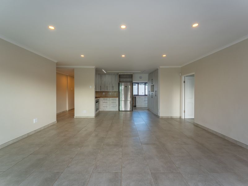 Spacious open-plan living area featuring neutral tiled flooring, recessed downlights, and a modern kitchen with built-in cabinetry and stainless steel appliances.