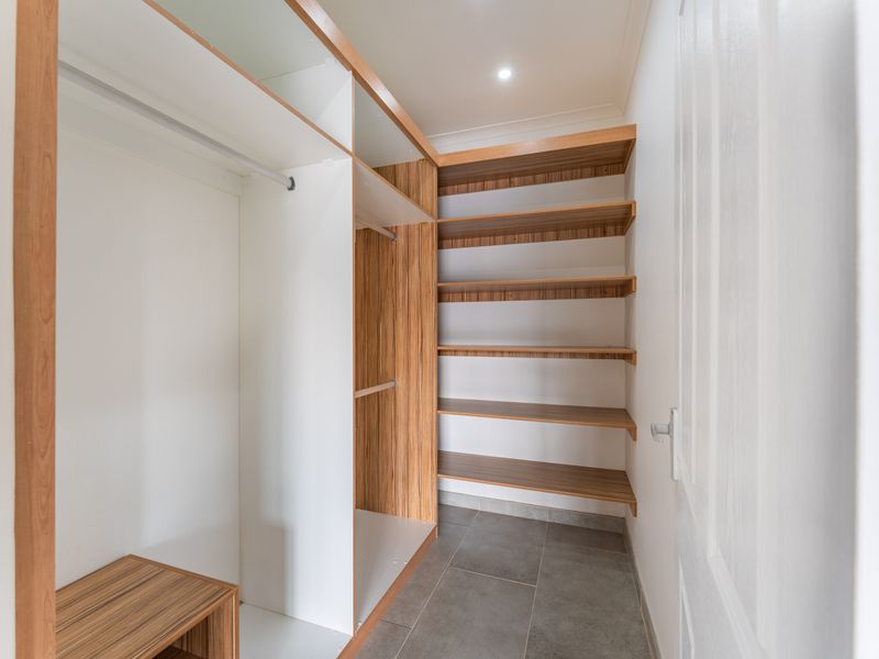 A clean, modern walk-in storage or utility space featuring custom built-in shelving, hanging rails, and durable tiled flooring.