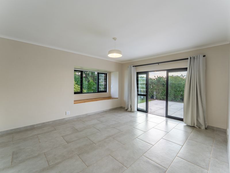 A bright, empty living room featuring neutral tiled floors, a built-in window seat, and sliding glass doors providing direct access to the outdoor patio area.