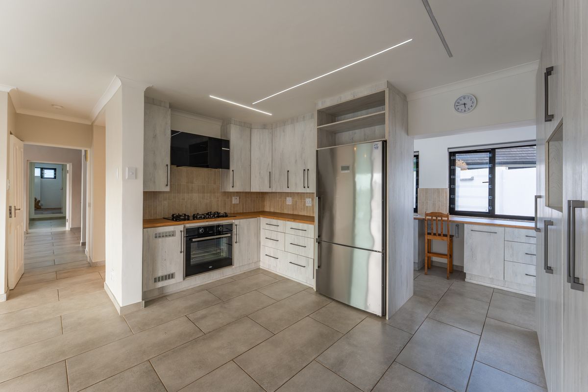 Modern kitchen featuring light wood-grain cabinetry, built-in oven and gas hob, tiled flooring, and sleek recessed linear lighting.