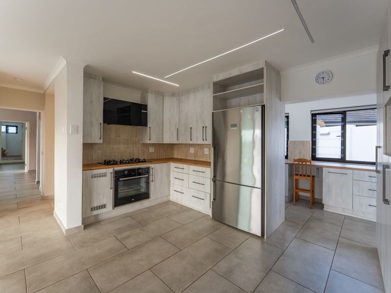 Modern kitchen featuring light wood-grain cabinetry, built-in oven and gas hob, tiled flooring, and sleek recessed linear lighting.