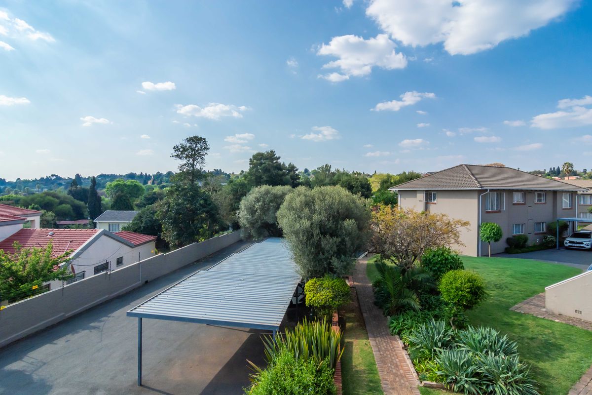 Aerial view of the townhouse complex grounds, featuring a covered carport, paved walkways, and well-maintained landscaped garden areas.