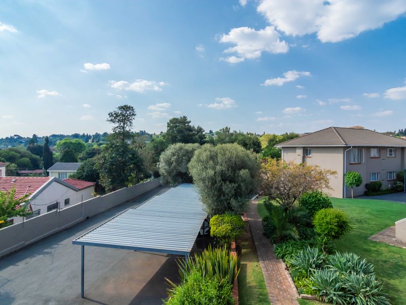 Aerial view of the townhouse complex grounds, featuring a covered carport, paved walkways, and well-maintained landscaped garden areas.