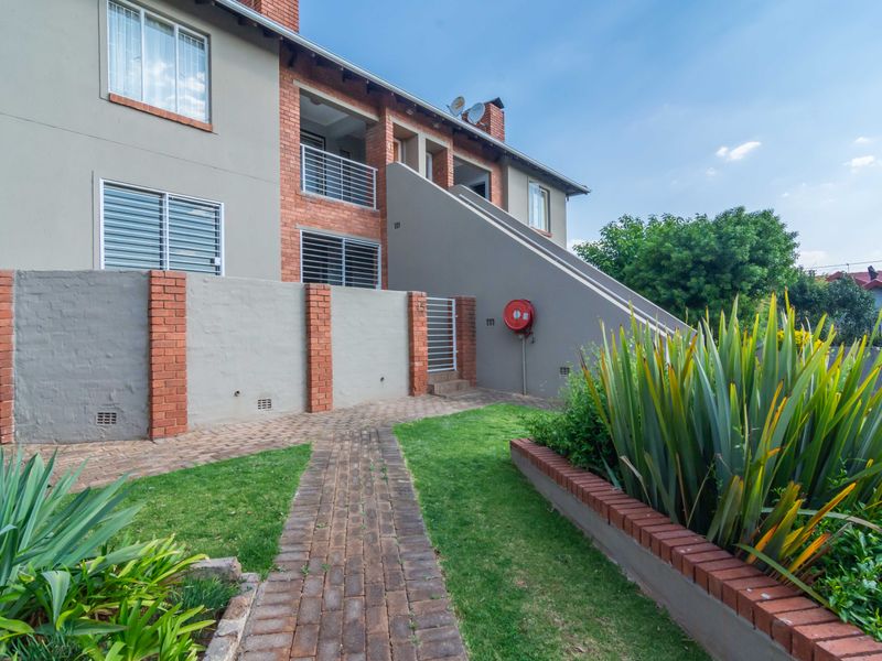 Front exterior view of a townhouse featuring a brick and rendered facade, paved walkway, landscaped garden, and balcony access.