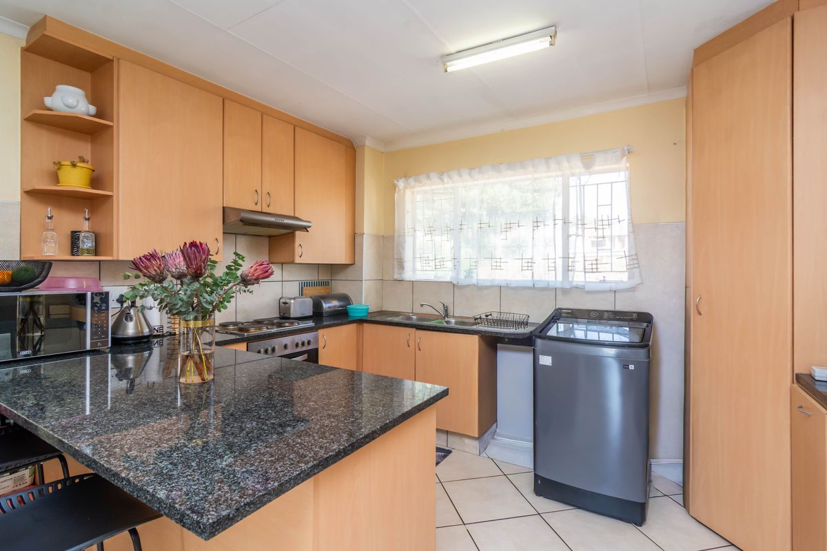 Functional kitchen featuring granite countertops, ample built-in cabinetry, an electric hob with extractor fan, and tiled flooring.