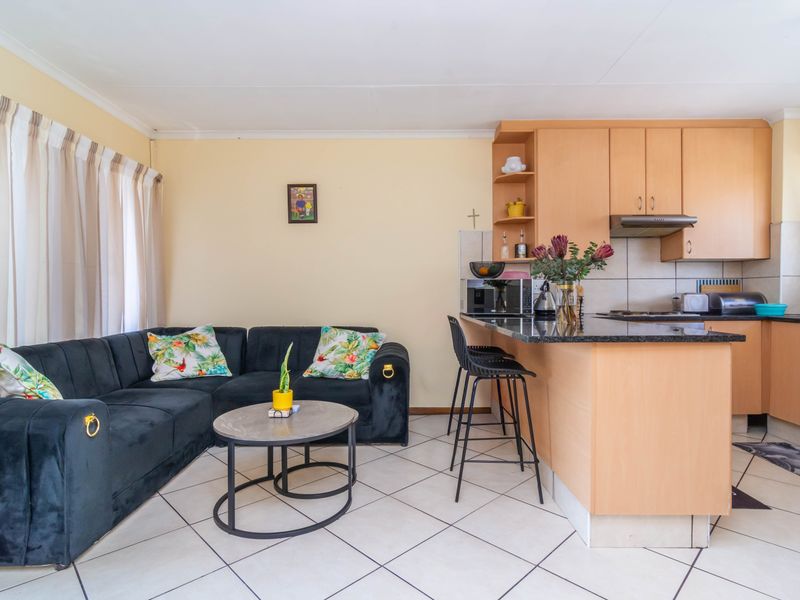 Open-plan living area featuring a functional kitchen with light wood cabinetry, granite countertops, and tiled flooring throughout the combined space.