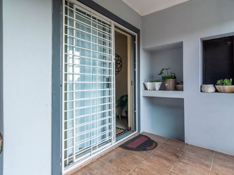 A covered patio area featuring tiled flooring, a sliding glass door with a security gate, and a built-in wall niche for display.