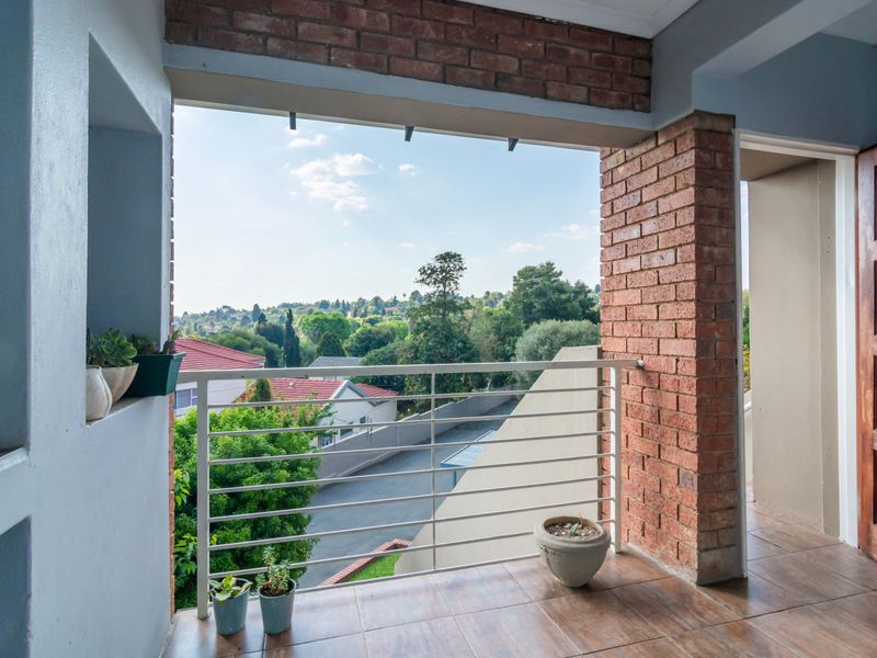 A covered balcony featuring brick pillars, tiled flooring, and a metal balustrade, offering an elevated view of the surrounding neighborhood.