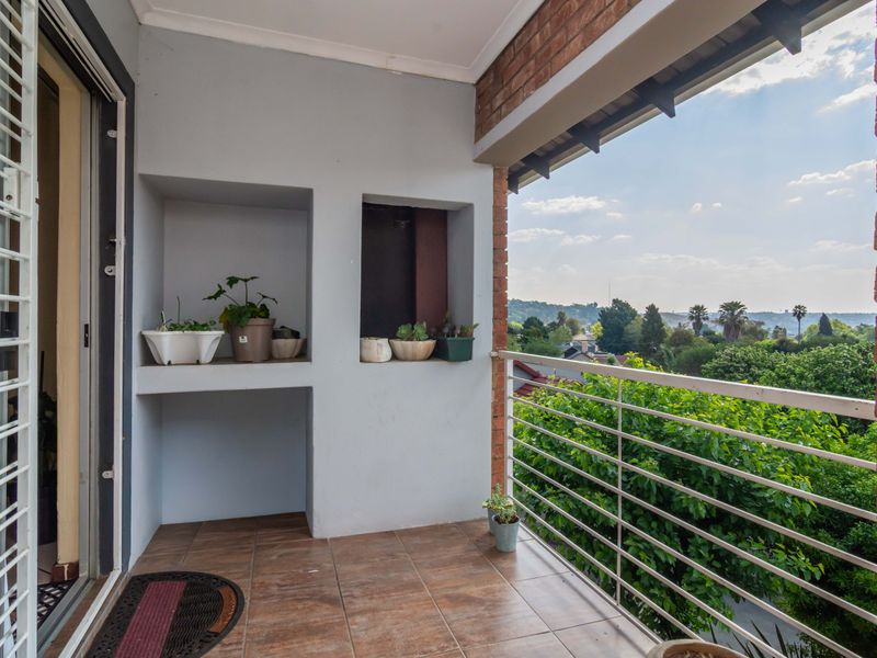 A covered balcony featuring tiled flooring, built-in wall niches, and a metal balustrade, offering elevated views of the surrounding neighborhood and greenery.
