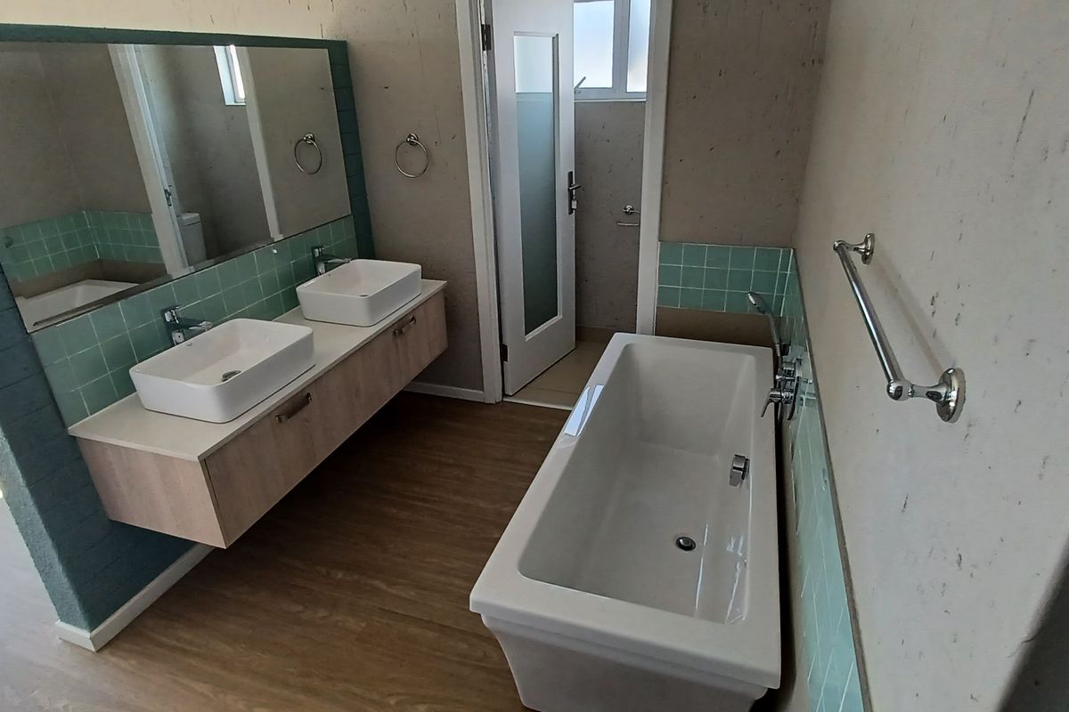 Modern bathroom featuring a double vanity with vessel sinks, a freestanding bathtub, and contemporary tiled splashbacks in a neutral, well-lit space.