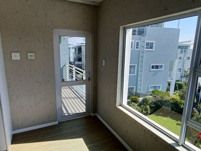 An empty bedroom featuring laminate flooring, built-in cupboards, and a door leading to a balcony with views of the surrounding complex.