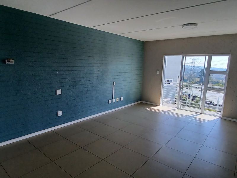 Spacious, empty living area featuring large format floor tiles, a striking blue accent wall, and a sliding door leading to an outdoor balcony.