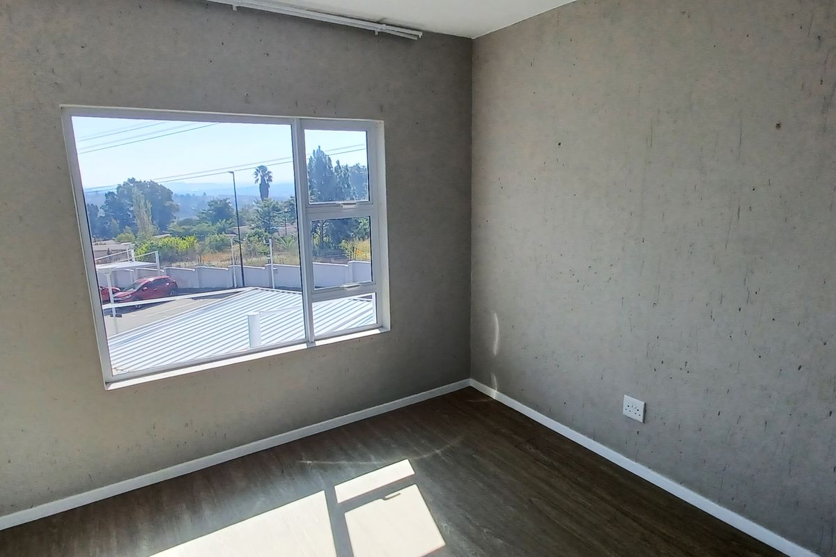 An empty bedroom featuring laminate flooring, aluminium window frames, and wall surfaces requiring cosmetic attention.