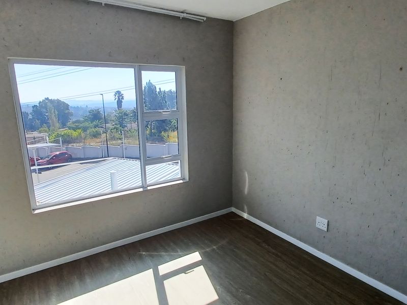An empty bedroom featuring laminate flooring, aluminium window frames, and wall surfaces requiring cosmetic attention.