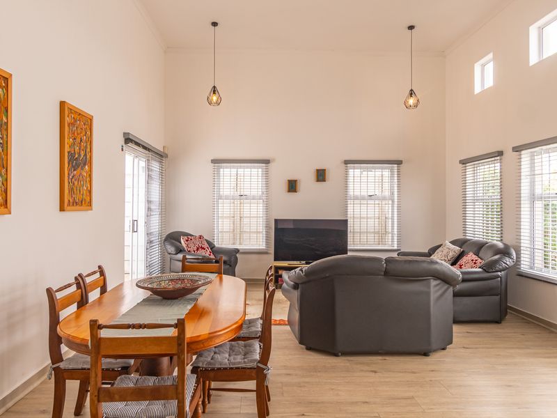 Spacious open-plan living and dining area featuring high ceilings, laminate flooring, large windows with venetian blinds, and modern pendant lighting.
