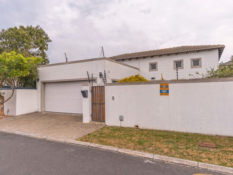 Front exterior view of the property featuring a paved driveway, automated garage, and secure boundary wall with electric fencing.