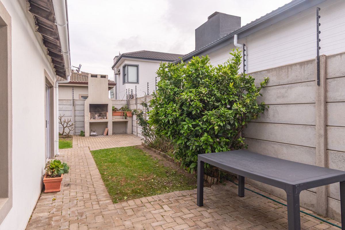 A private rear courtyard featuring a paved patio area, a built-in braai, and secure perimeter walling with electric fencing.