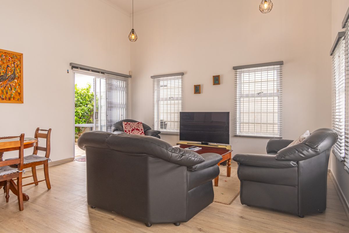 A bright living room featuring laminate flooring, high ceilings, pendant lighting, and sliding glass doors leading to an outdoor area with security gates.