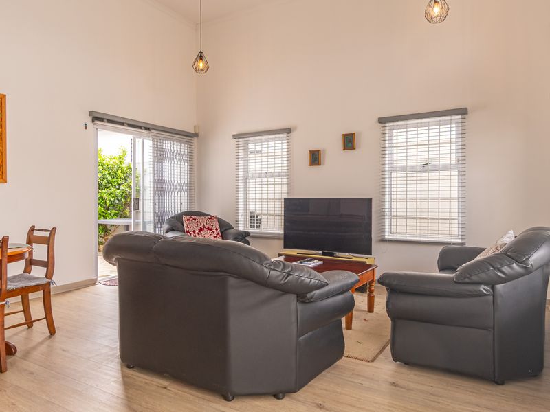 A bright living room featuring laminate flooring, high ceilings, pendant lighting, and sliding glass doors leading to an outdoor area with security gates.