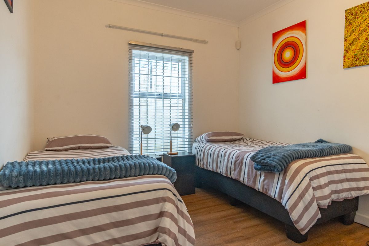 A functional bedroom featuring laminate flooring, a central window with venetian blinds, and neutral wall finishes.