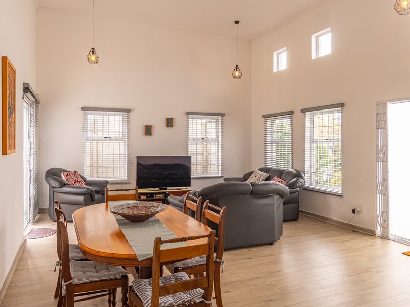Spacious open-plan living and dining area featuring high ceilings, laminate flooring, abundant natural light through multiple windows, and direct access to the exterior.