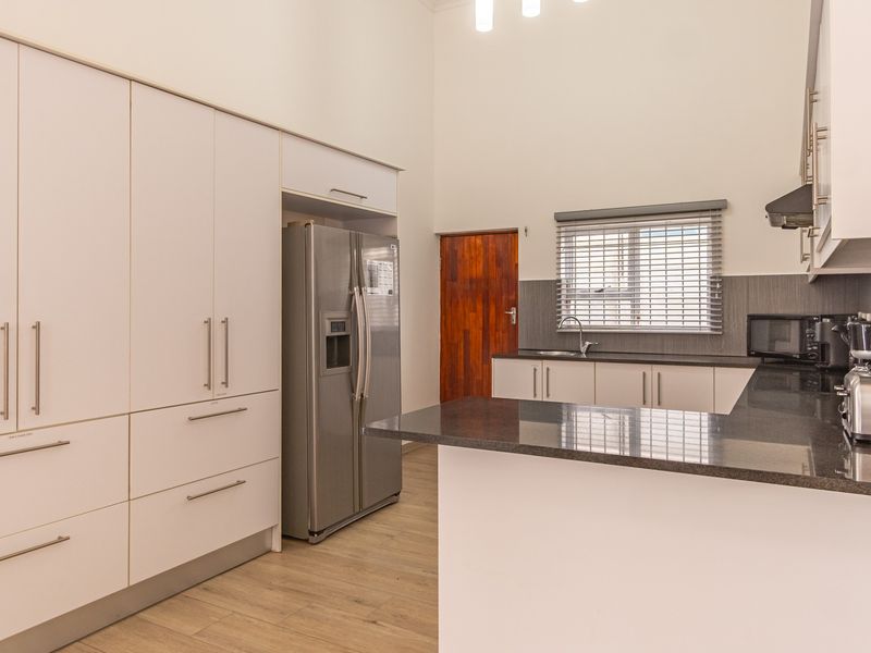 Modern kitchen featuring ample built-in cabinetry, granite countertops, stainless steel sink, and extractor fan, complemented by light-toned laminate flooring.